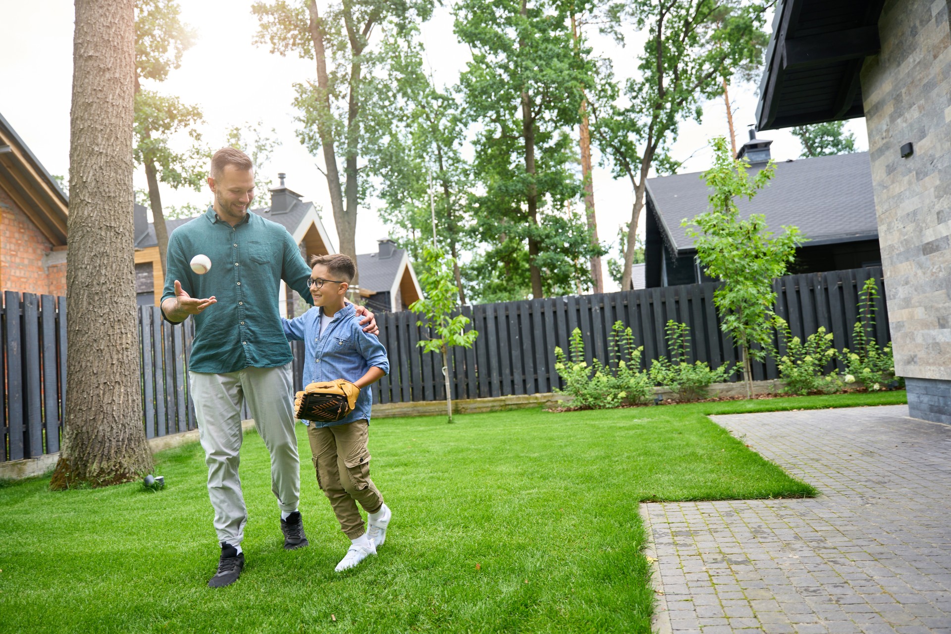 Man and boy are walking along green grass near house